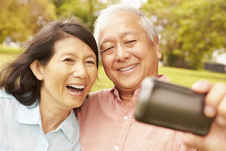 Older Asian couple smiling for a selfie with dentures making their smiles look perfect and camera ready.