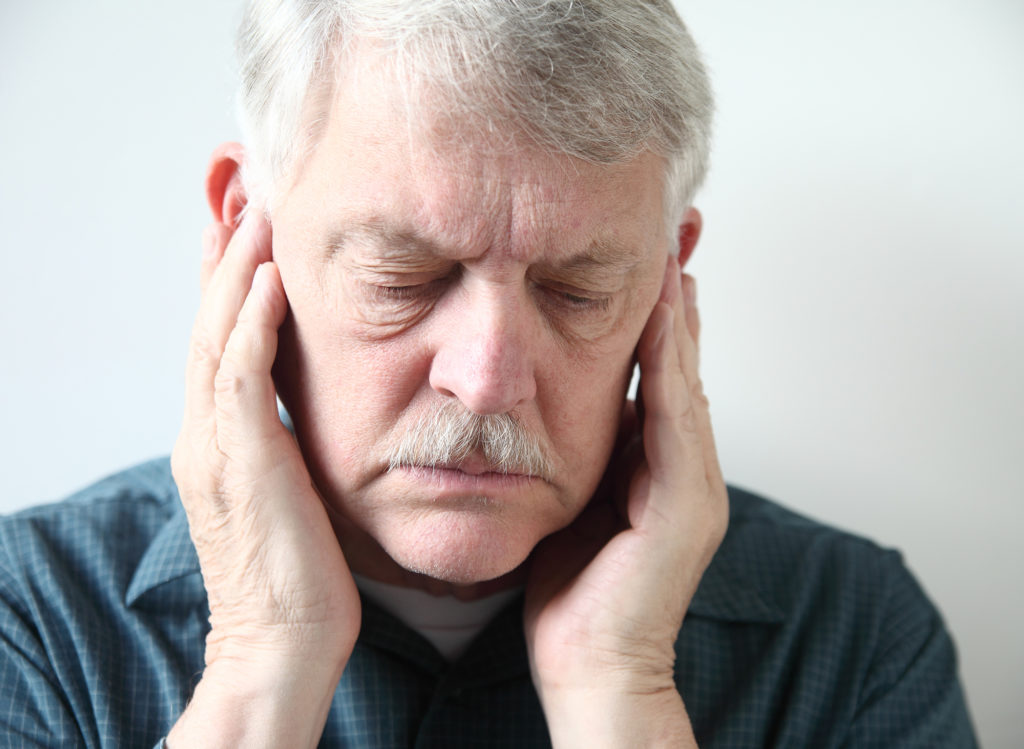 Man holding his ears because of pain which is a common symptom of TMJ which you can be screened for at Chris Johns, DDS in Millbrae, CA.