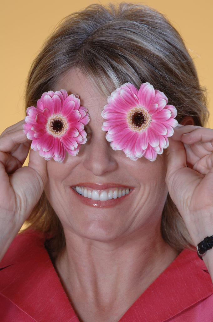 Woman playfully holding flowers in front of her eyes and smiling with a perfect smile from dental implants. 